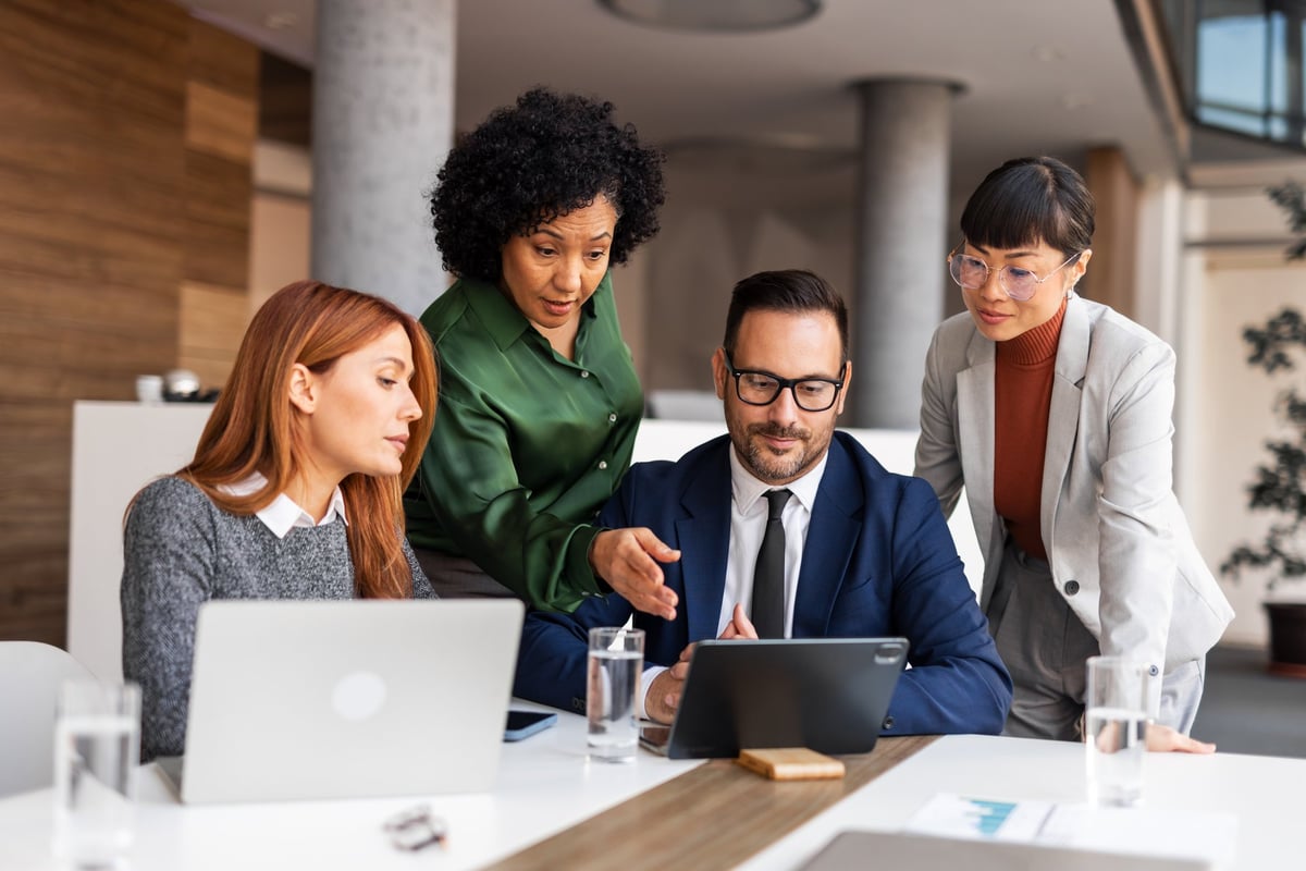 Professionals collaborate in a modern office environment with laptops and tablets, fostering teamwork and productivity. Participants engage in discussions and planning activities while showcasing a business-oriented atmosphere.